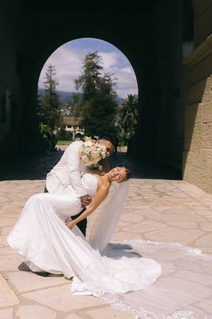 Bride and groom share a romantic dip kiss under an arched doorway at an outdoor wedding venue.