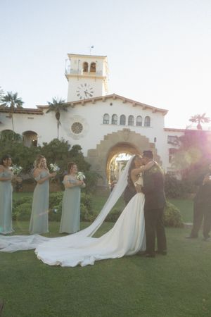 Bride and groom kissing at outdoor wedding ceremony with bridesmaids in sage green dresses at Santa Barbara Courthouse.