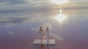 Silhouetted figures sit on a dock at sunset with vibrant orange and purple clouds reflecting on calm waters.