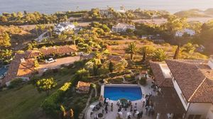 Aerial panoramic view of a luxury resort with swimming pools and palm trees at sunset in a coastal setting.