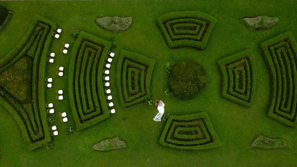 Aerial view of a symmetrical garden maze with geometric patterns and curved pathways on lush green grass.