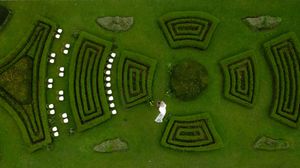 Aerial view of a symmetrical garden maze with geometric patterns and curved pathways on lush green grass.