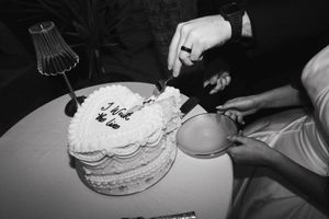 A black and white photo shows hands cutting into a decorated birthday cake with a small lamp in the background.