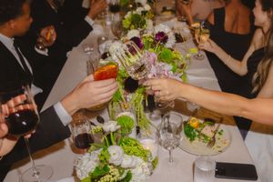 Guests raise champagne glasses in a toast at an elegant dinner table decorated with floral centerpieces and wine glasses.