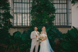 A couple shares a romantic moment in front of a white building with ornate windows and lush greenery.
