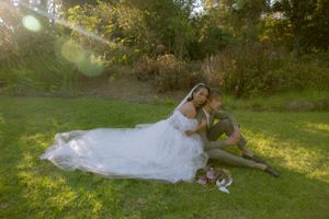 A couple in wedding attire lays together in a sunlit grassy field during a romantic outdoor photo session.