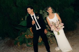 Wedding party walks through a dark wooded area at night while holding bouquets and wearing formal attire.