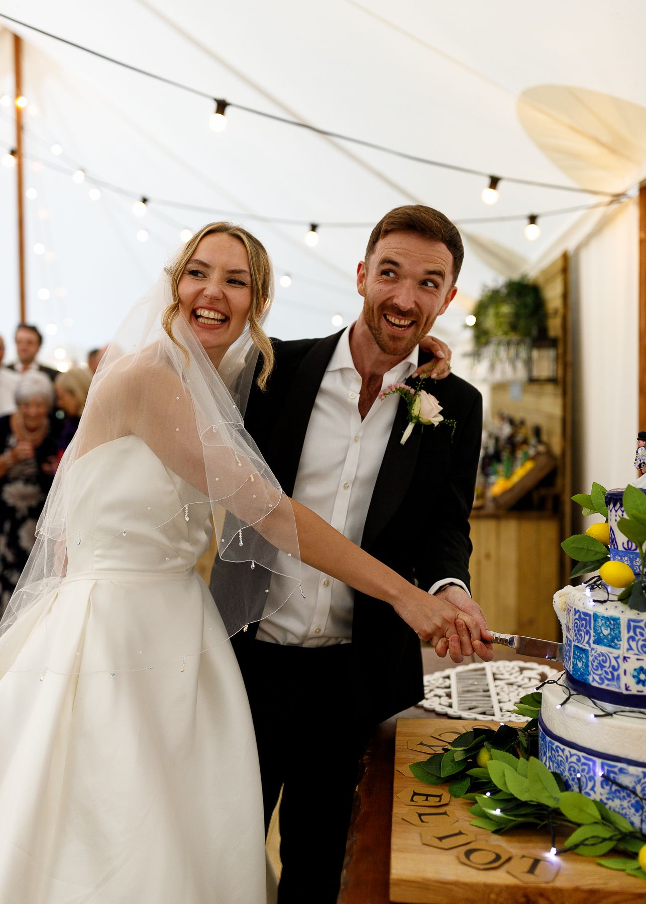 A couple cuts their wedding cake together in a tent reception decorated with blue and white china details.