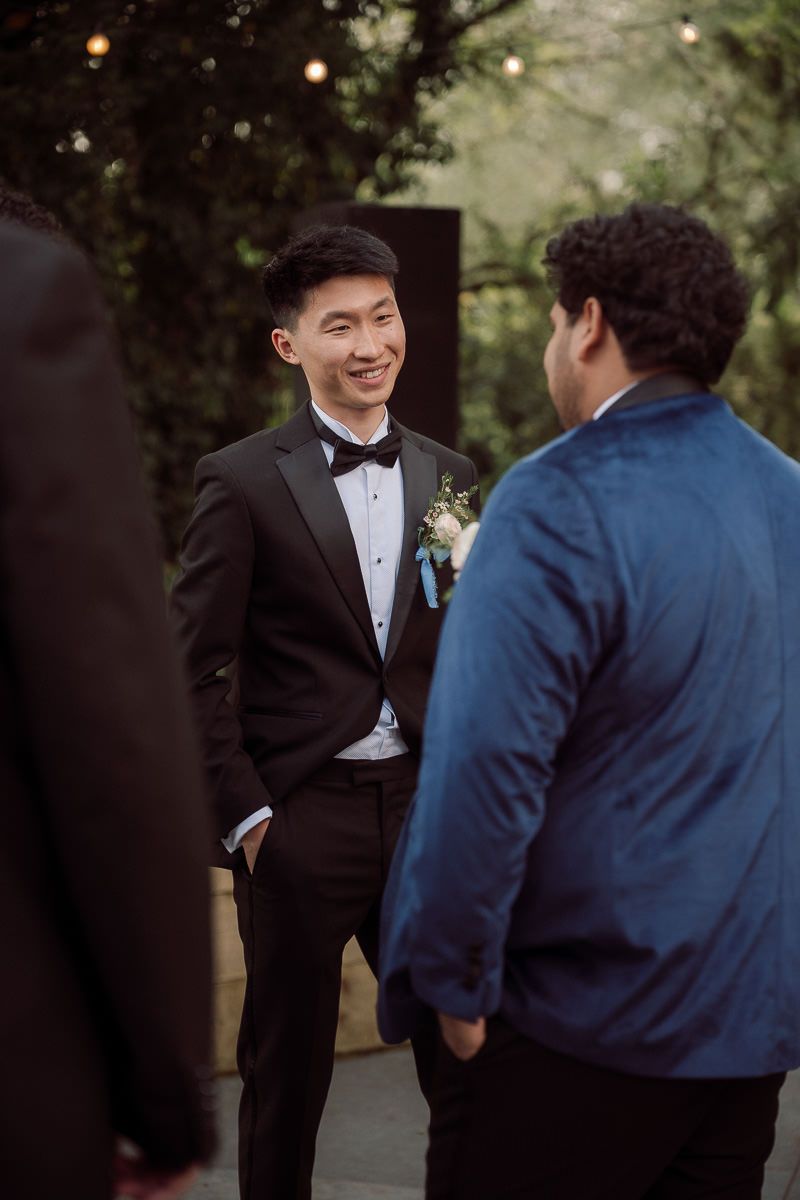 Two people in formal attire share a candid moment during what appears to be a wedding celebration outdoors.