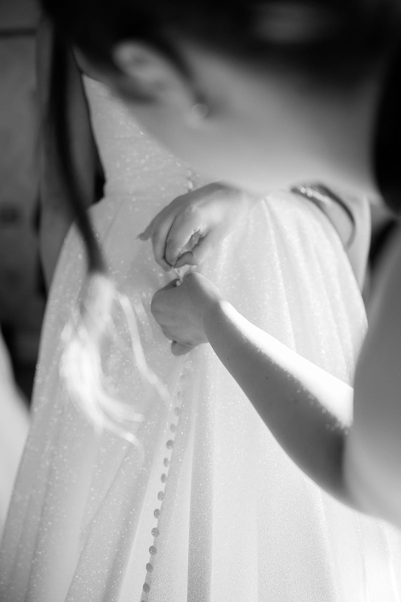 A series of black and white close-up photos showing delicate details of a white wedding dress with buttons and fabric textures.