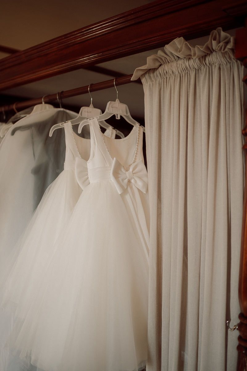 White wedding dresses hanging on a rod against cream curtains in a dressing room.
