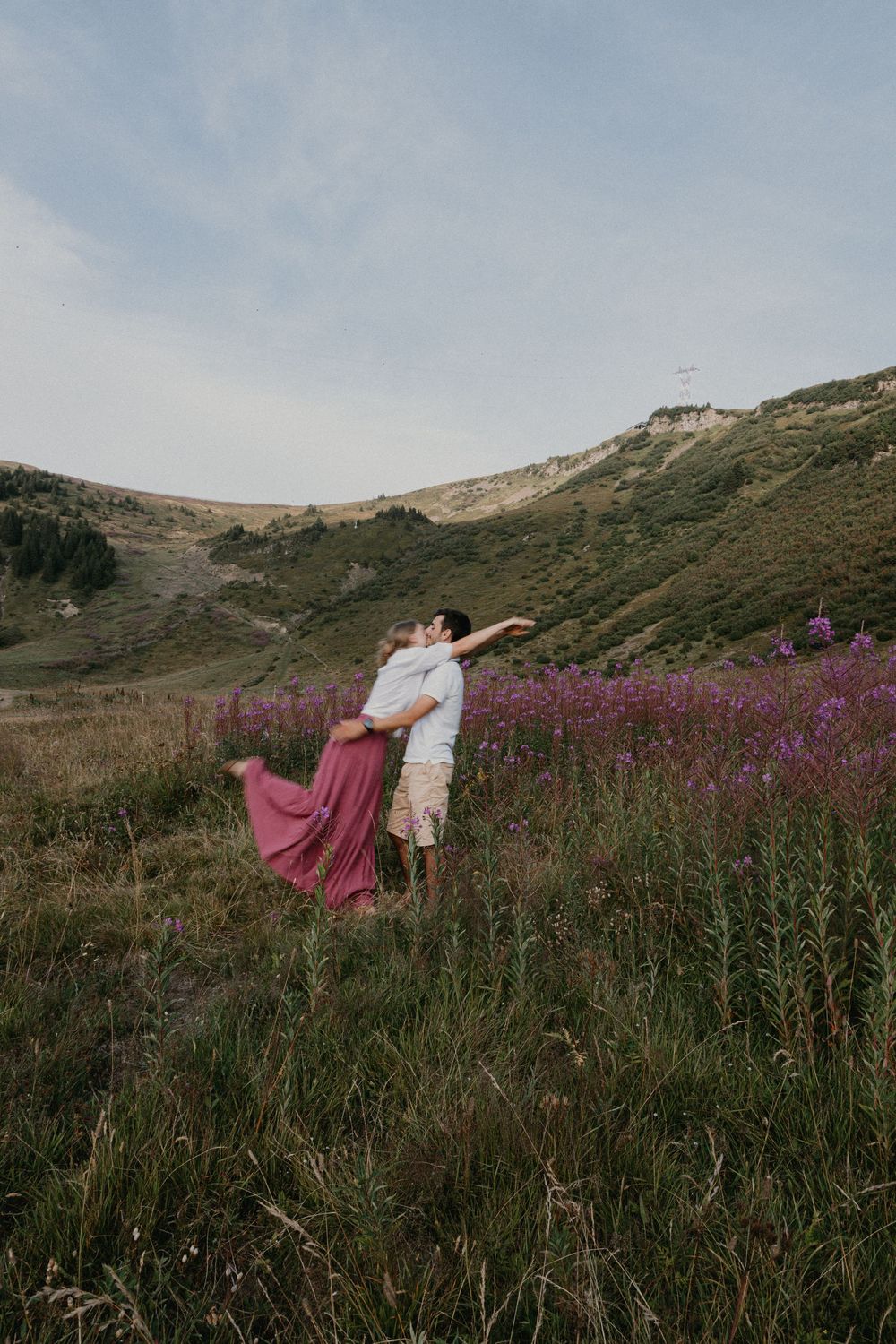 A couple dances in a field of vibrant purple wildflowers against a backdrop of rolling hills at sunset.