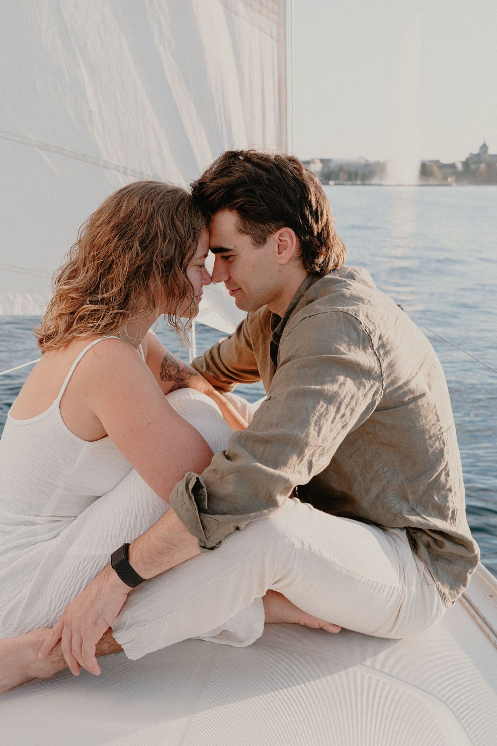A romantic couple shares an intimate moment while sitting on a boat during sunset on calm waters.