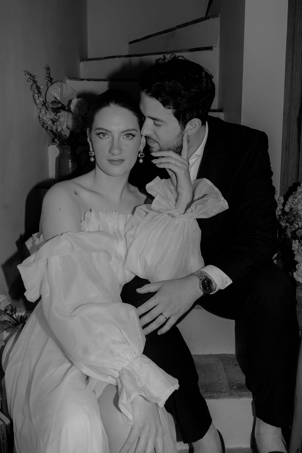 A romantic black and white photo of a couple in formal attire, with the woman in white and man in black suit.
