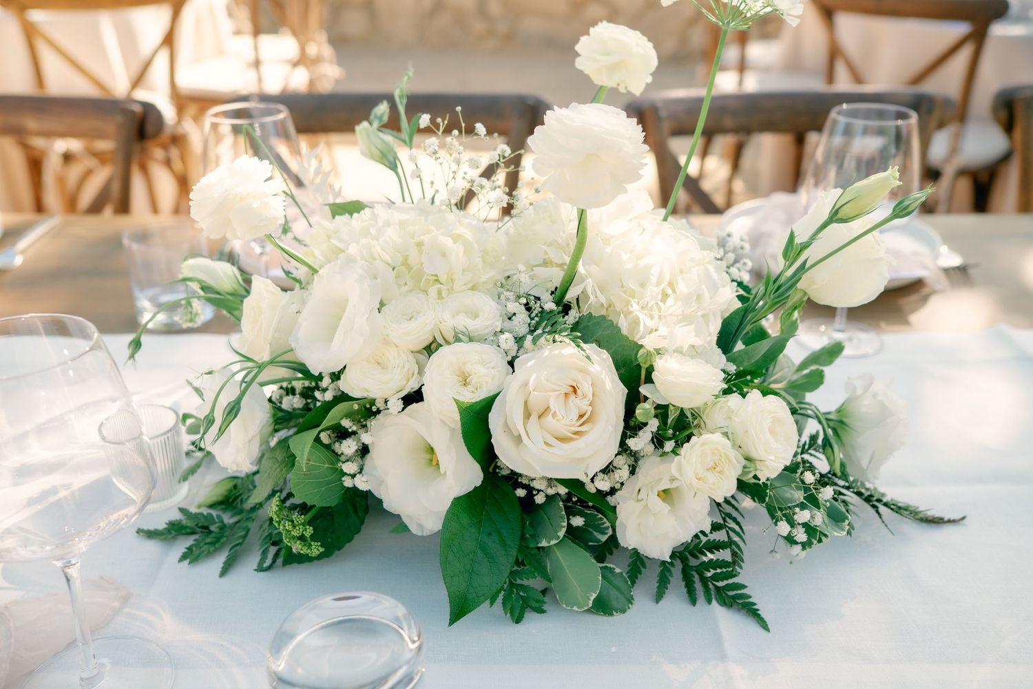 Elegant white floral centerpiece with roses and greenery arranged on a table at an indoor wedding reception.