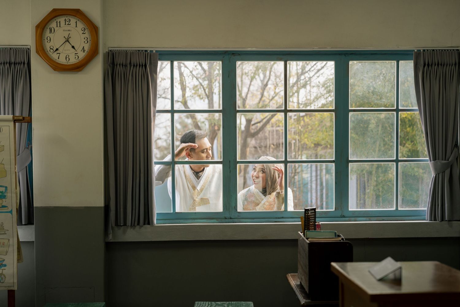 A modern classroom interior with large windows, gray curtains, and a wall clock showing natural daylight.