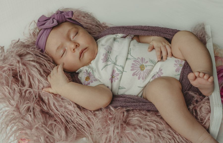 baby girl sleeping in baby bed wearing pink headband and a white onsie with pink flowers
in home newborn session