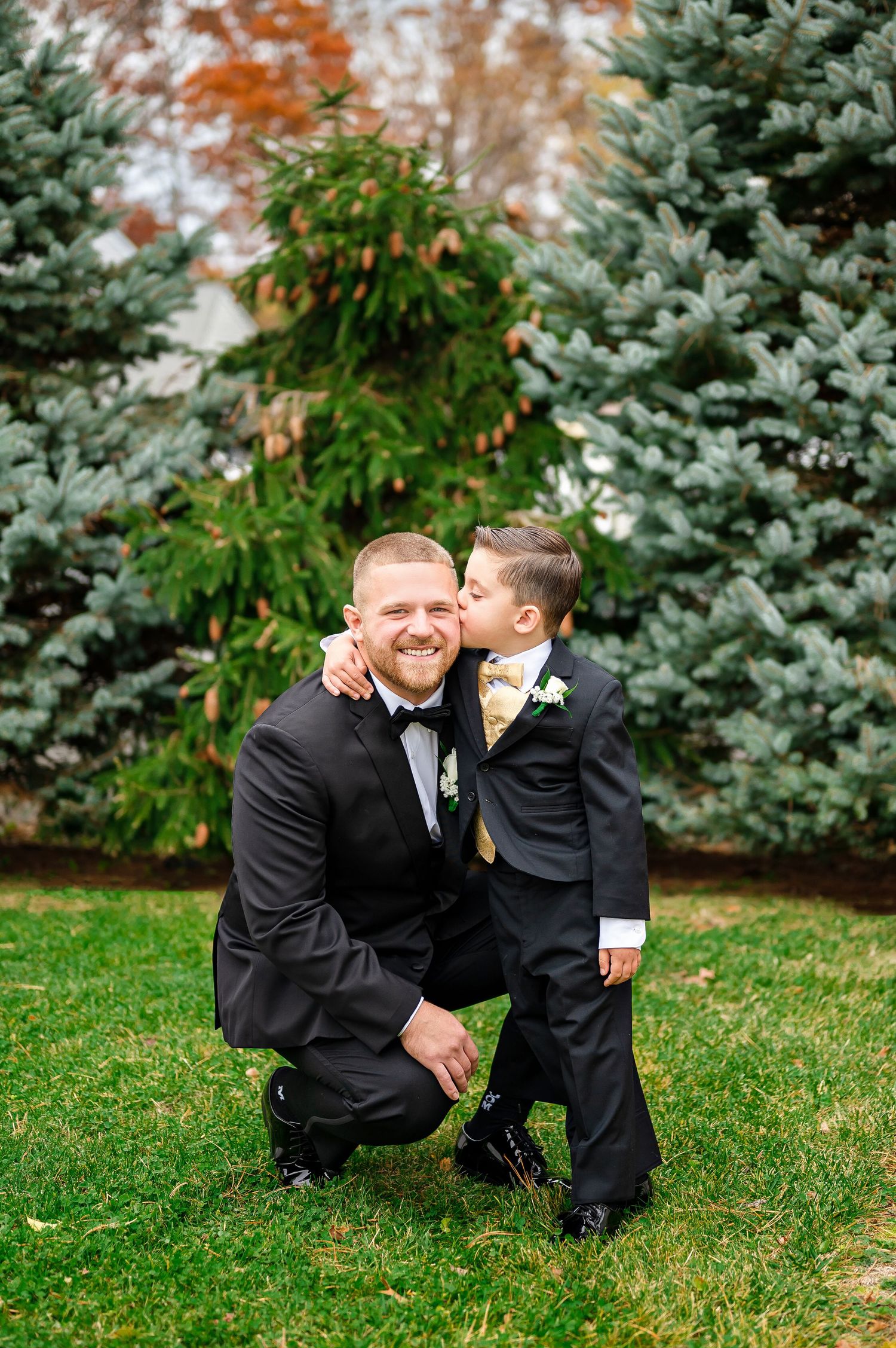 A couple embraces lovingly on a dirt path beside tall ornamental grasses on an overcast afternoon.