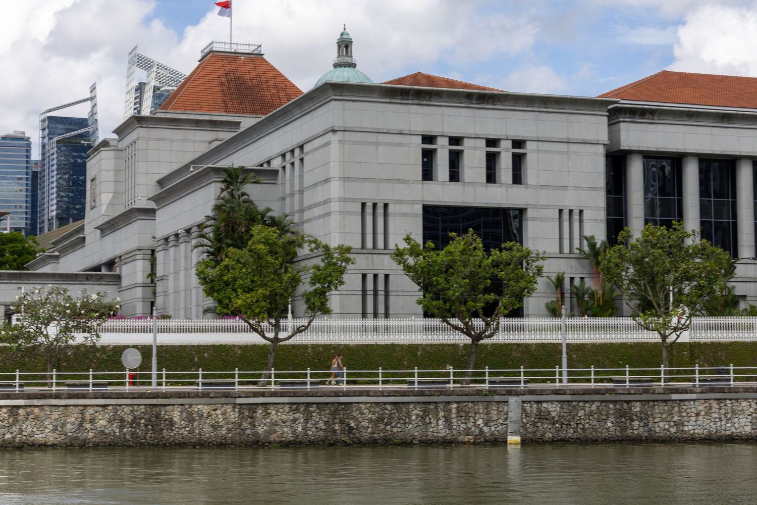Historic Parliament House building with white facade along Singapore River waterfront with modern skyline in background.
