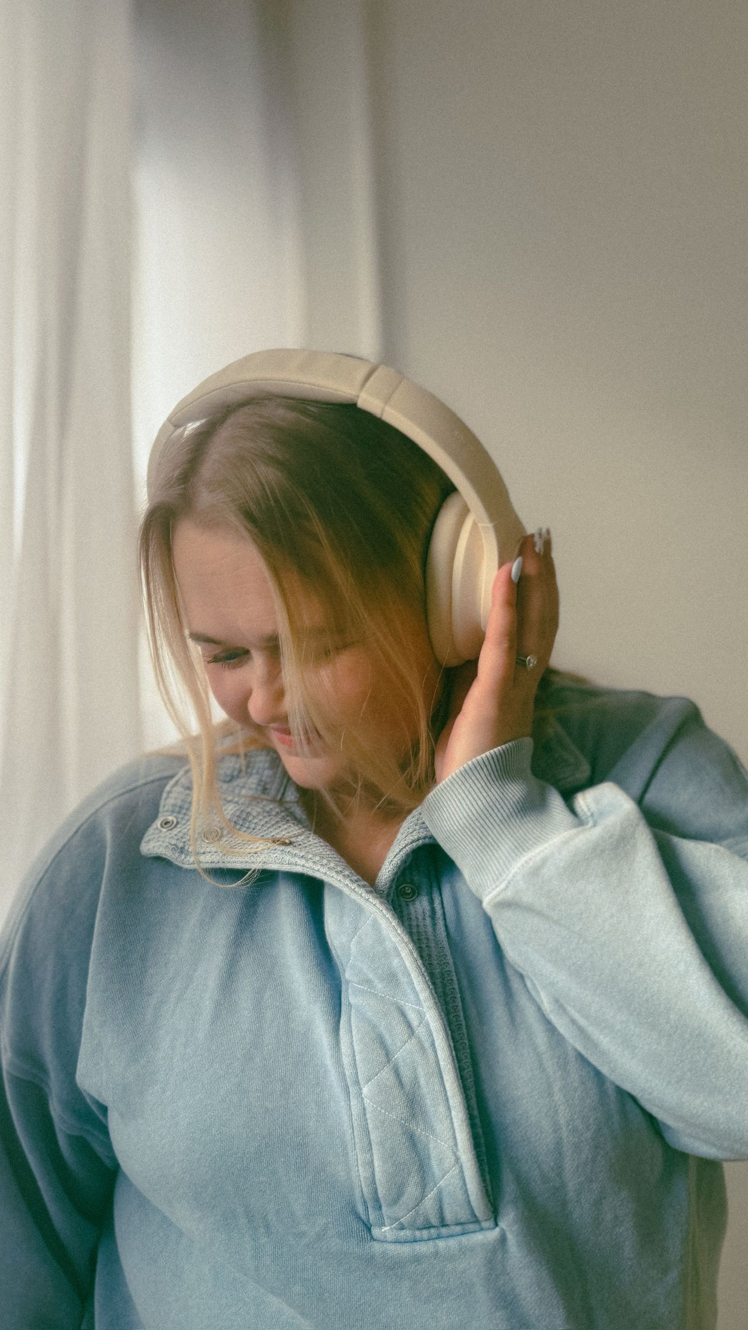Person in light blue denim wearing white headphones shown in a series of candid poses against a bright window.