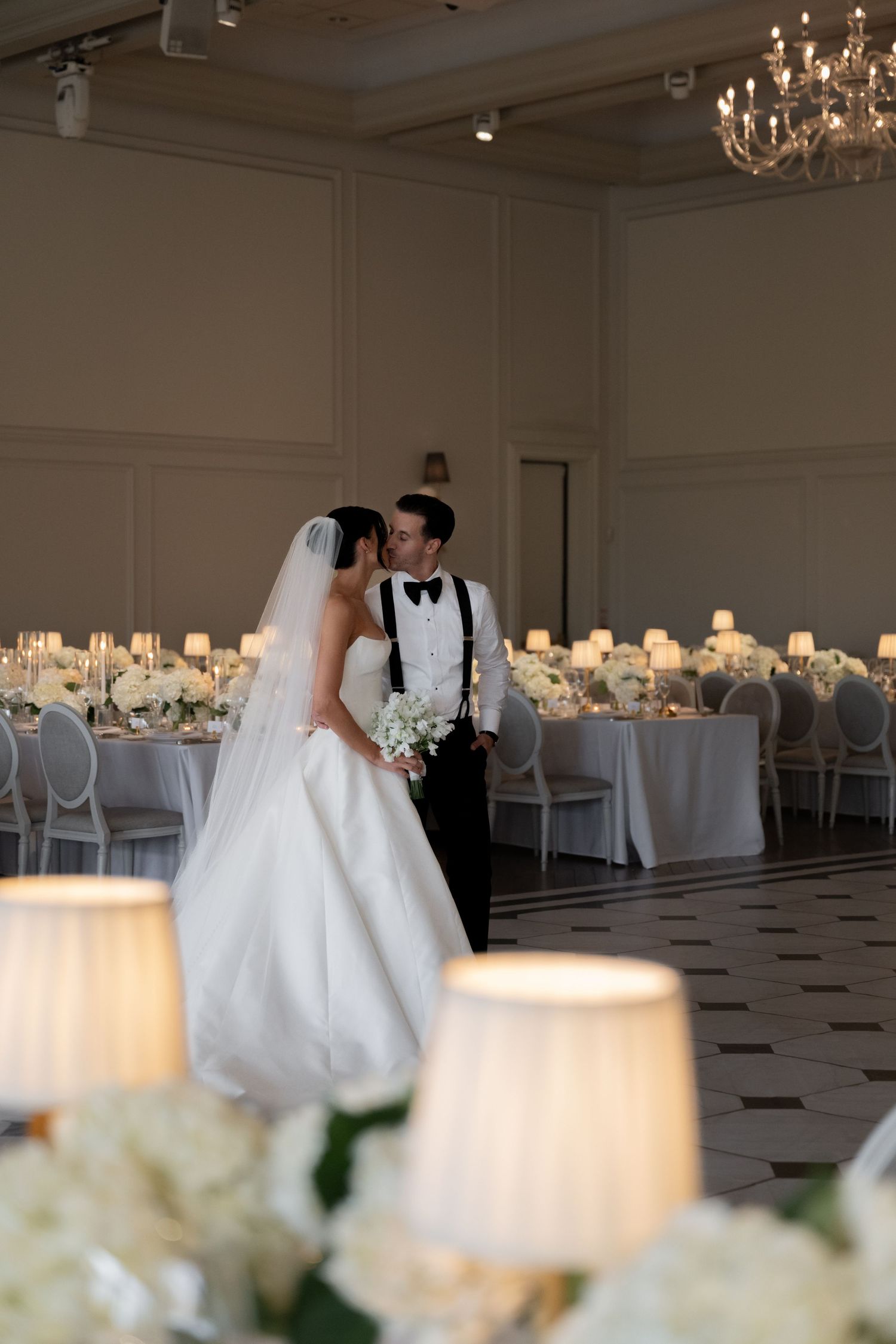 Elegant wedding reception ballroom with glowing table lamps and crystal chandelier creating romantic ambiance.