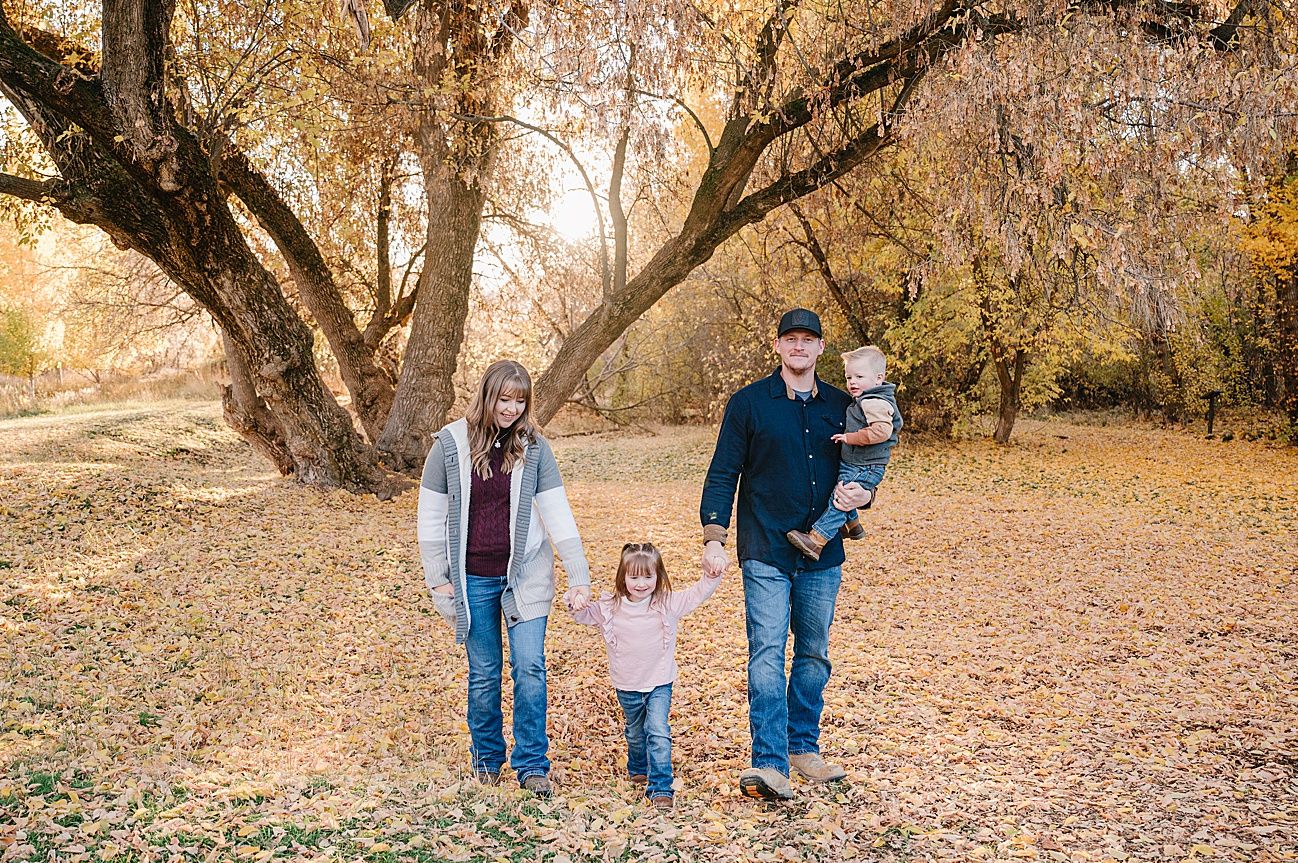 A family walking together through a fall landscape with golden leaves and sunlit trees.
