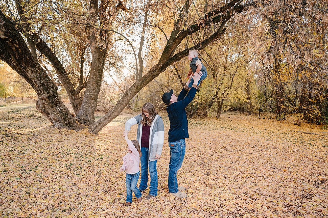 Family enjoying a fall photoshoot together in a park with golden autumn leaves scattered on the ground.