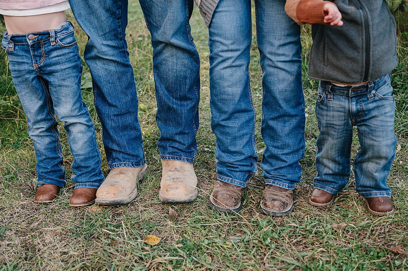 A row of people wearing blue jeans and boots standing in a line on grass showing just their legs and feet.