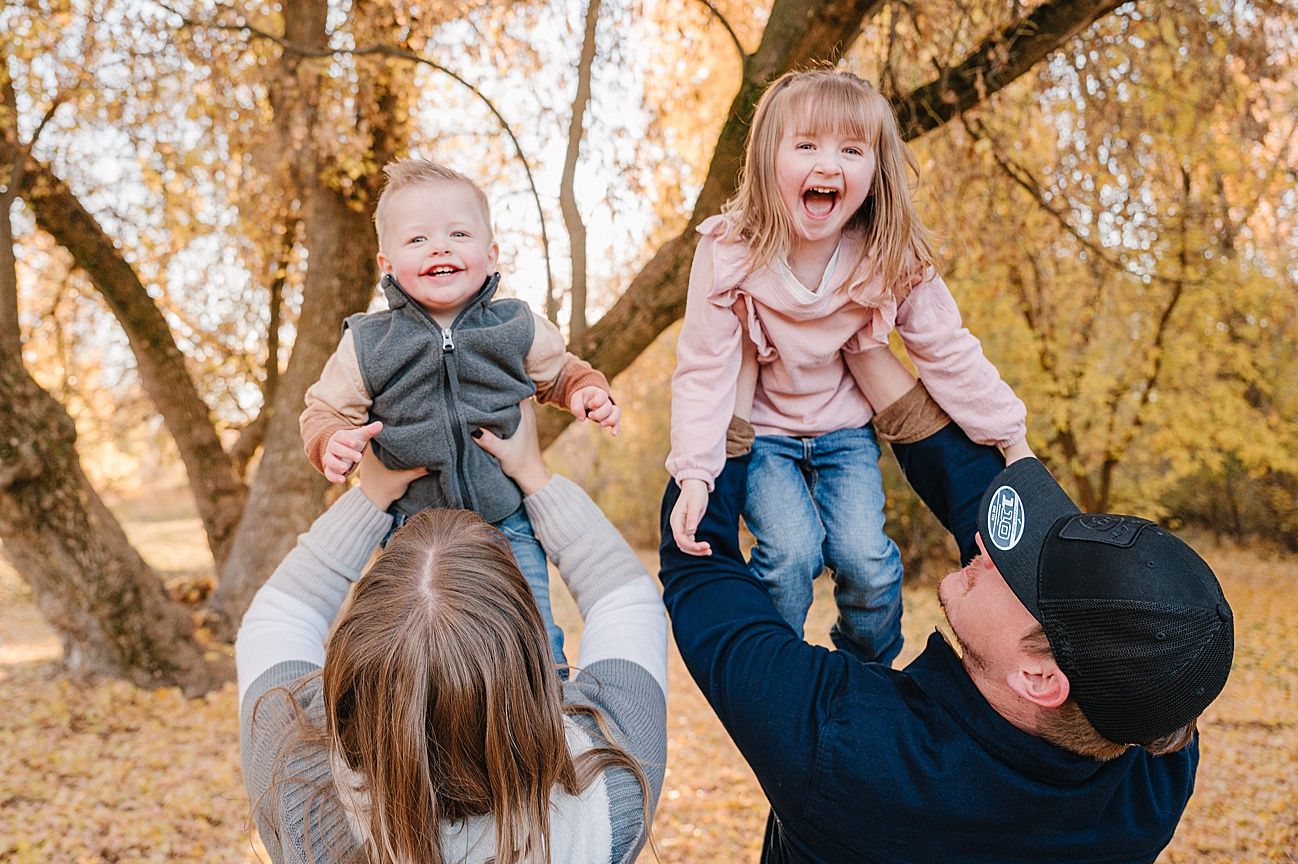 Family plays and laughs together during a golden autumn photo session in a park setting.