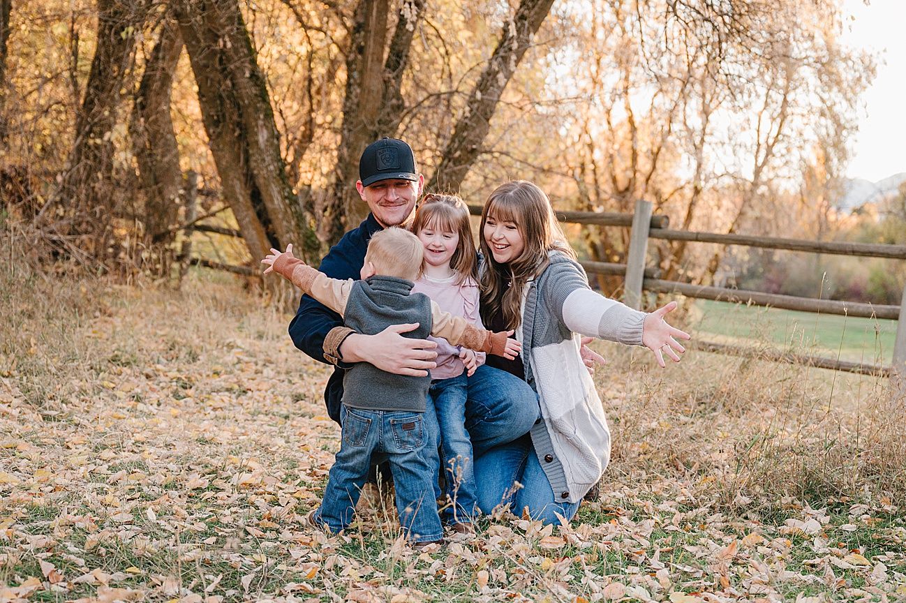 A family sits together on fallen autumn leaves in a wooded park during a golden sunset photoshoot.