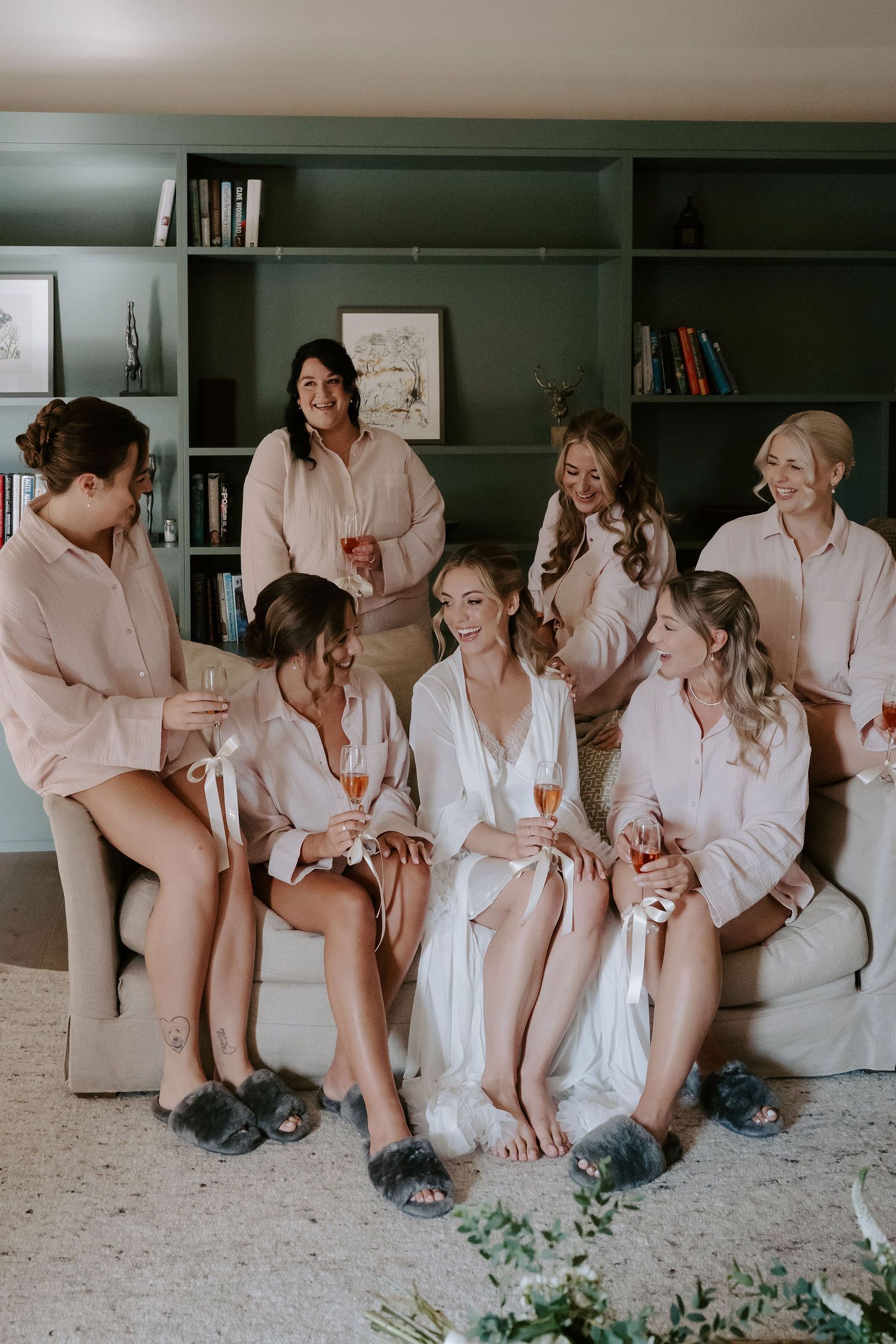 bride and bridesmaids sitting on sofa drinking champagne at ivy lodge in cirencester