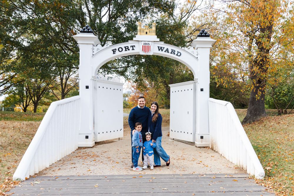 A family stands under the white Fort Warren entrance arch on an autumn day.