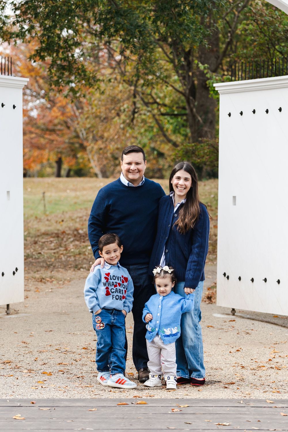 A family poses together in casual denim outfits near white walls during an autumn photoshoot.