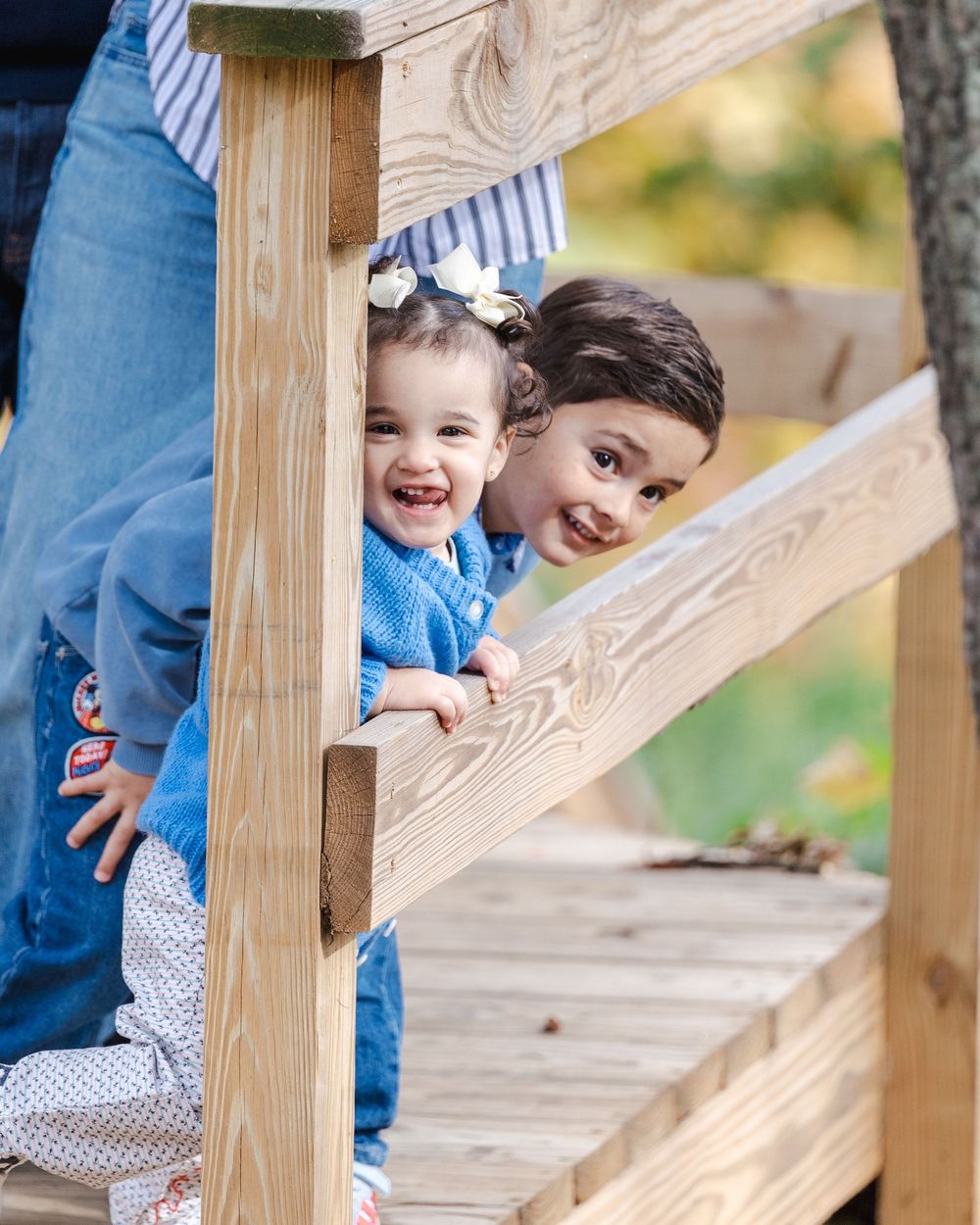 Children playfully peek through wooden fence slats in a candid outdoor moment.