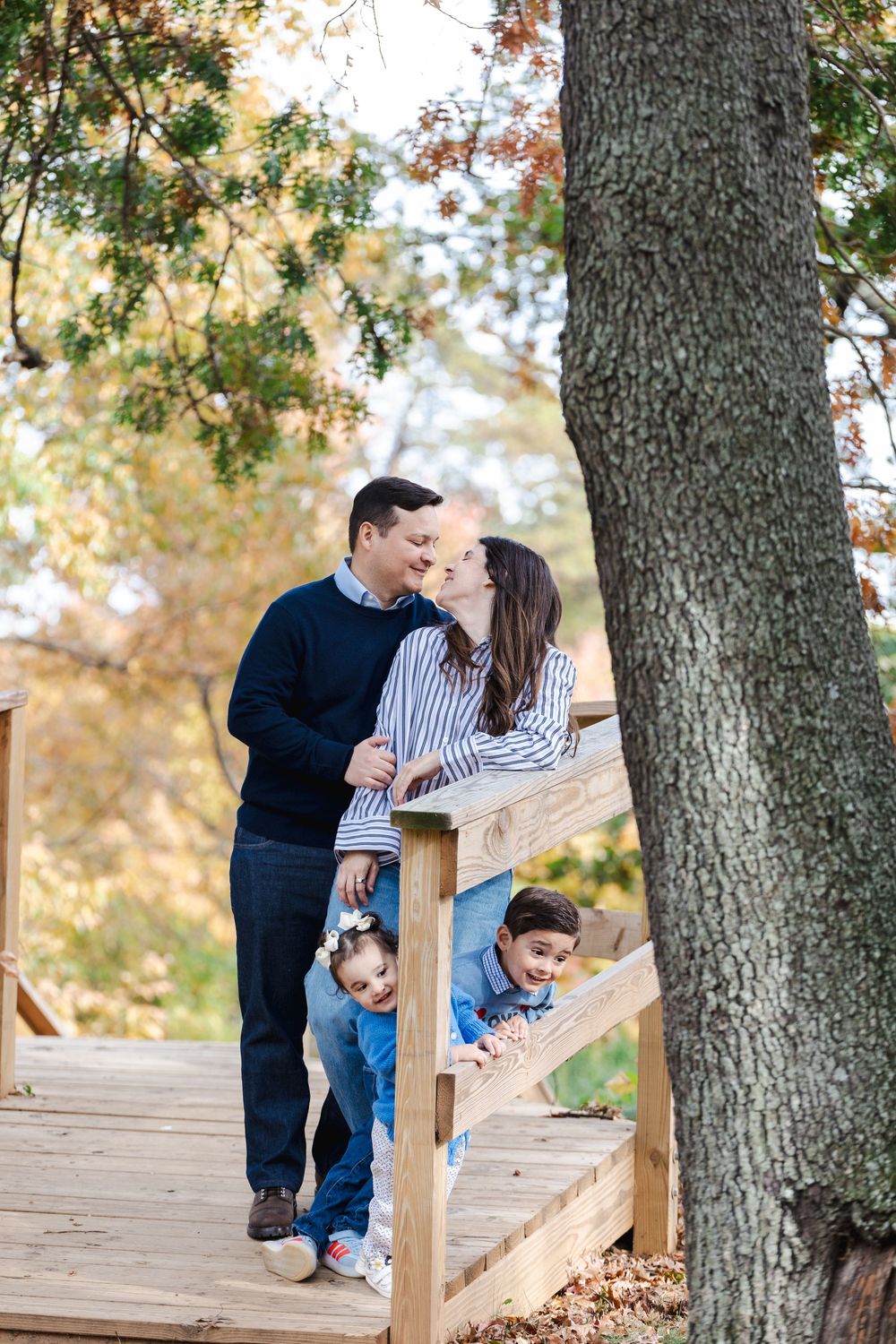 A couple shares an intimate moment while sitting on a wooden deck surrounded by autumn trees.