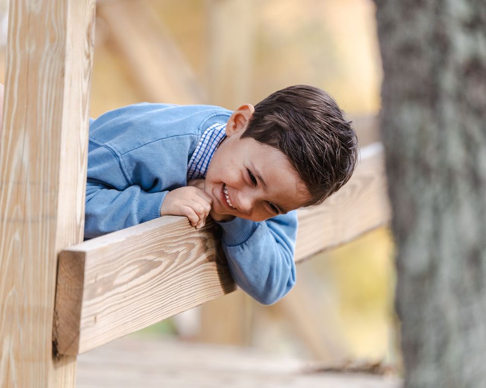 A person in a blue shirt peers through a wooden window frame in an outdoor setting.