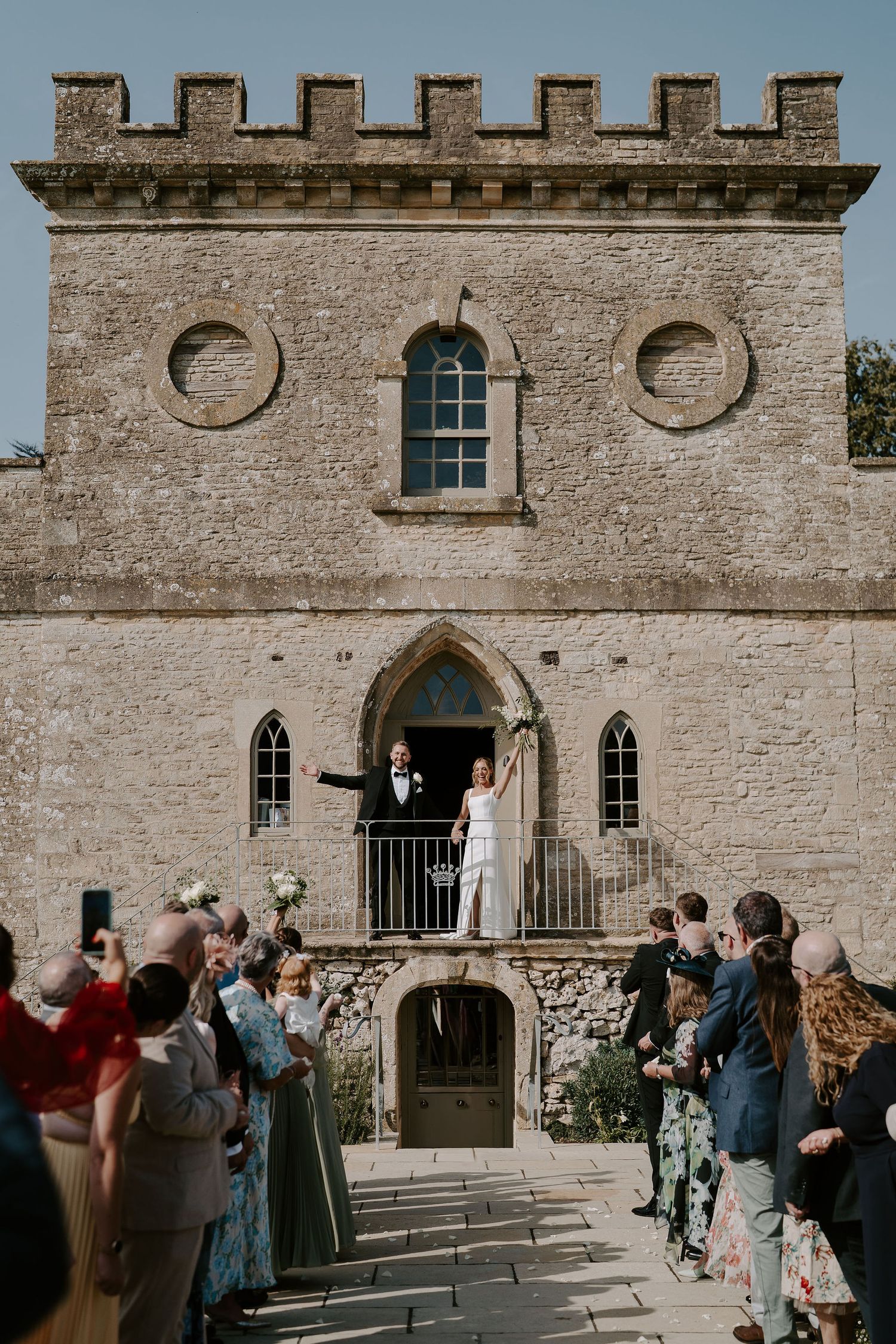 bride and groom waving at guests as they exit wedding ceremony at ivy lodge in cirencester