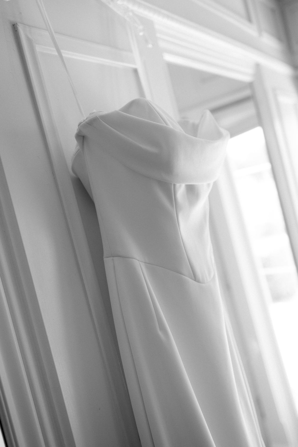 Elegant white wedding dress hanging by window in soft natural light.