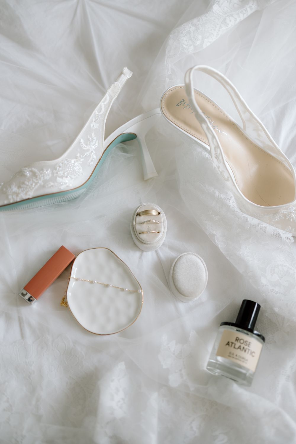 White bridal accessories including shoes, nail polish, and jewelry arranged on white fabric.