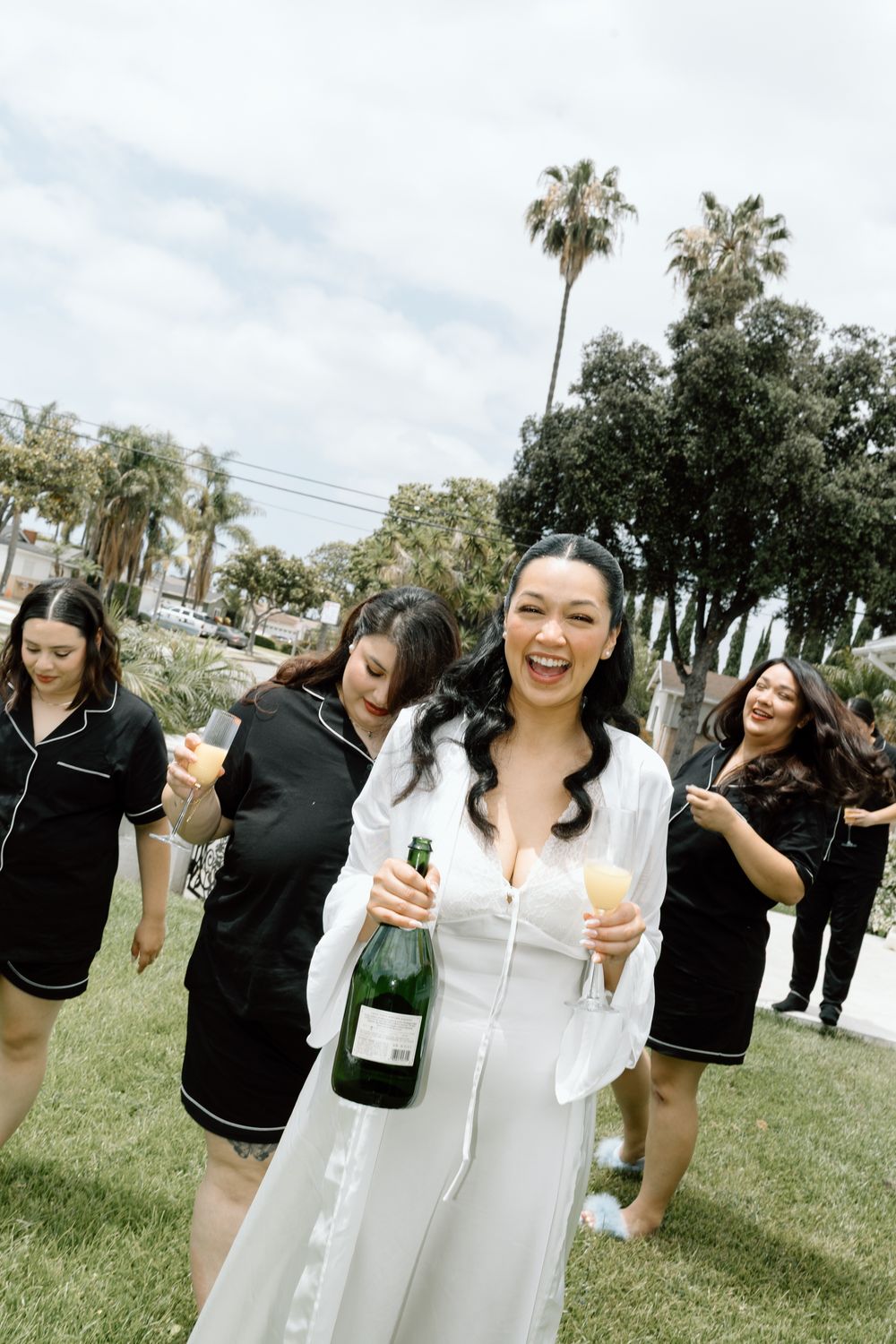 Group celebrating outdoors with champagne among palm trees.