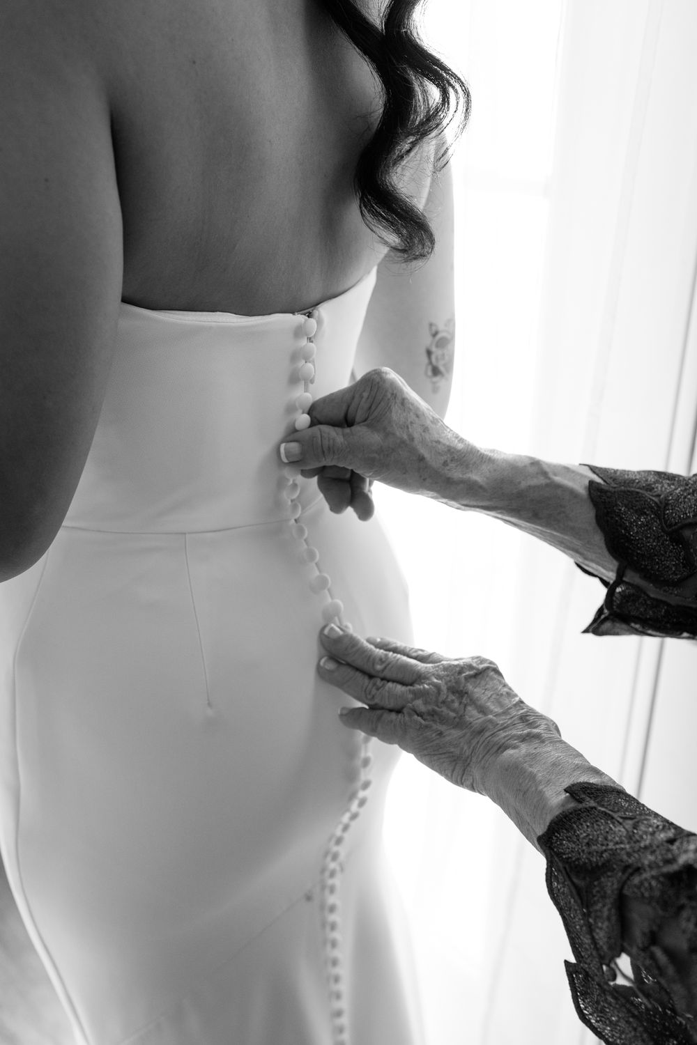 Close-up black and white photo of hands buttoning up a wedding dress.