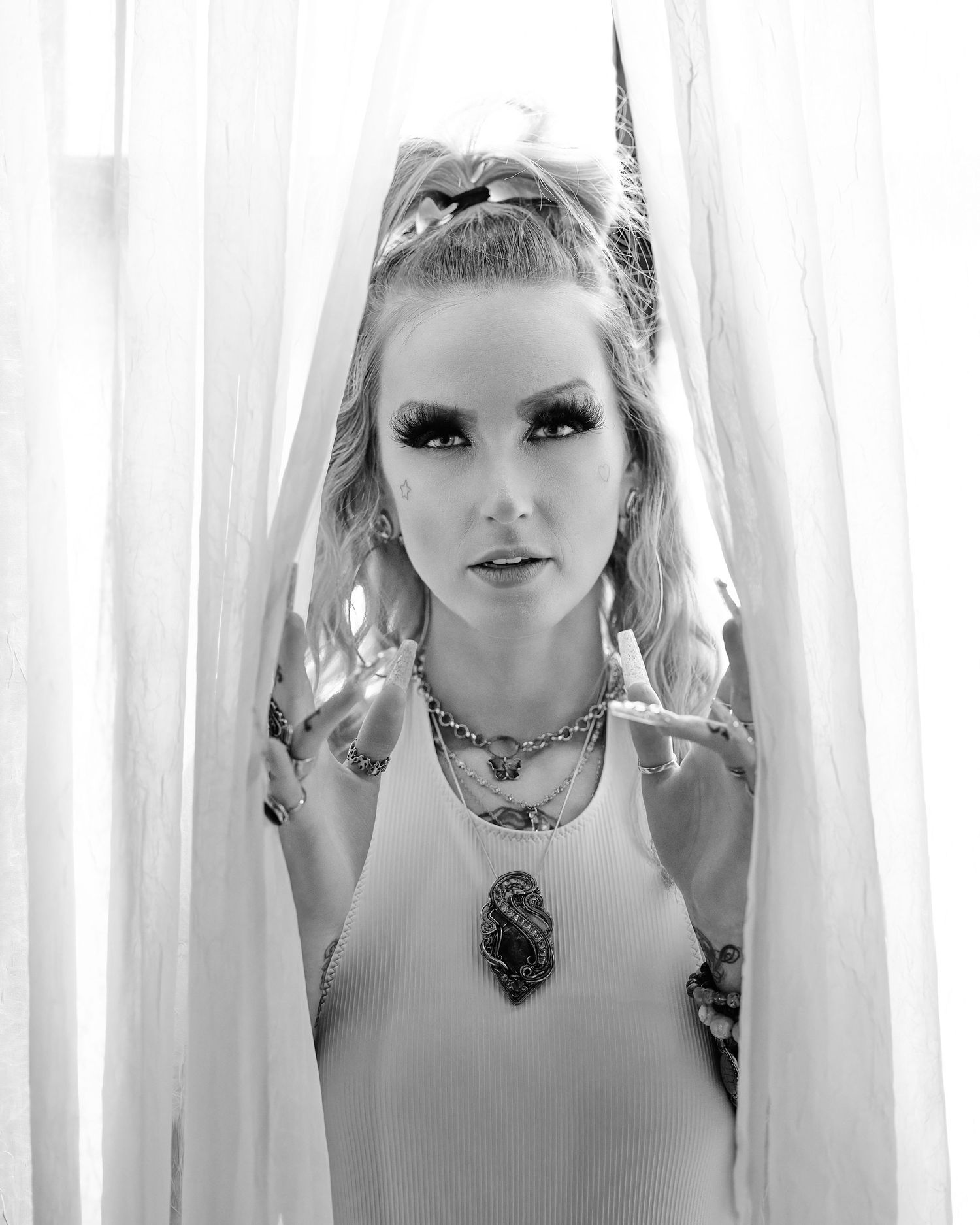 David G Holt Photography - A black and white artistic portrait through sheer curtains featuring dramatic makeup and ornate jewelry.