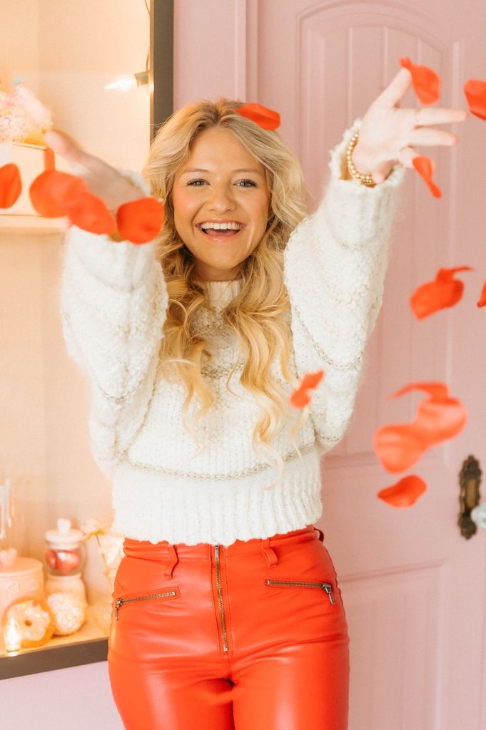 Woman in white sweater and red pants tossing heart confetti in Valentine's themed photo series.