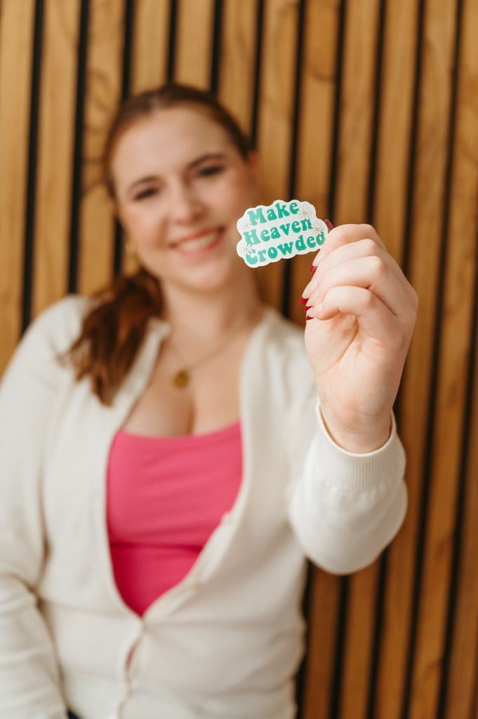 Person in white cardigan and pink top holding up a small decorative item.