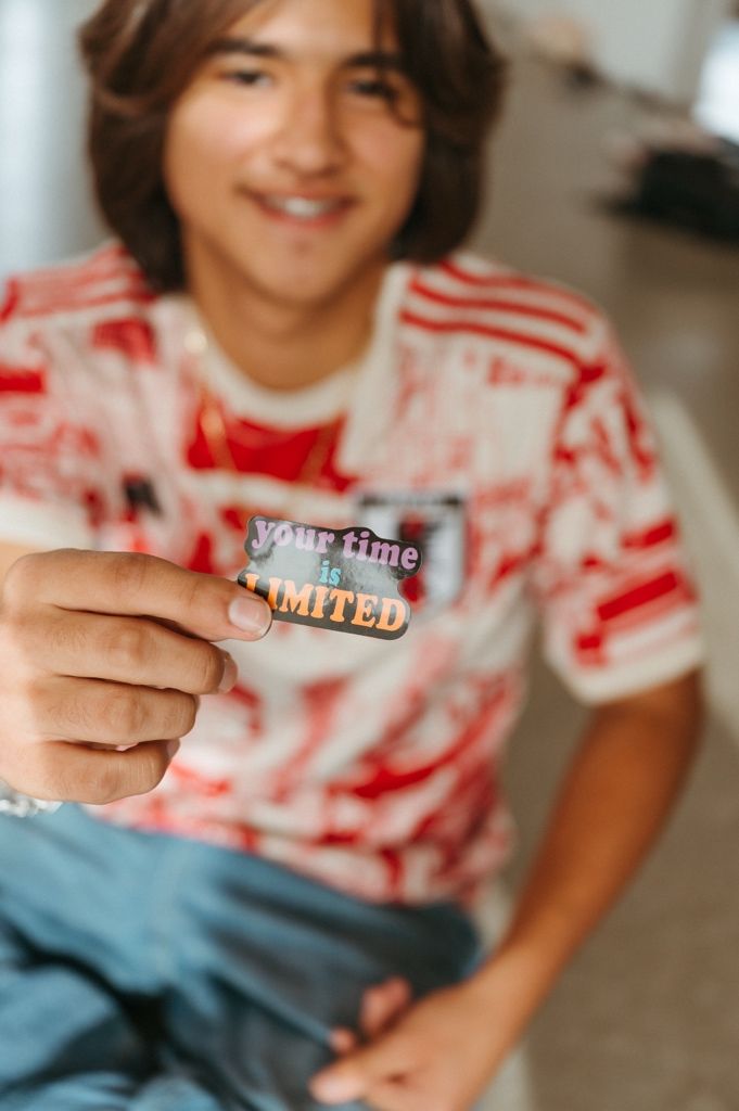 A close-up shot shows hands holding a small item while wearing a red and white patterned shirt.