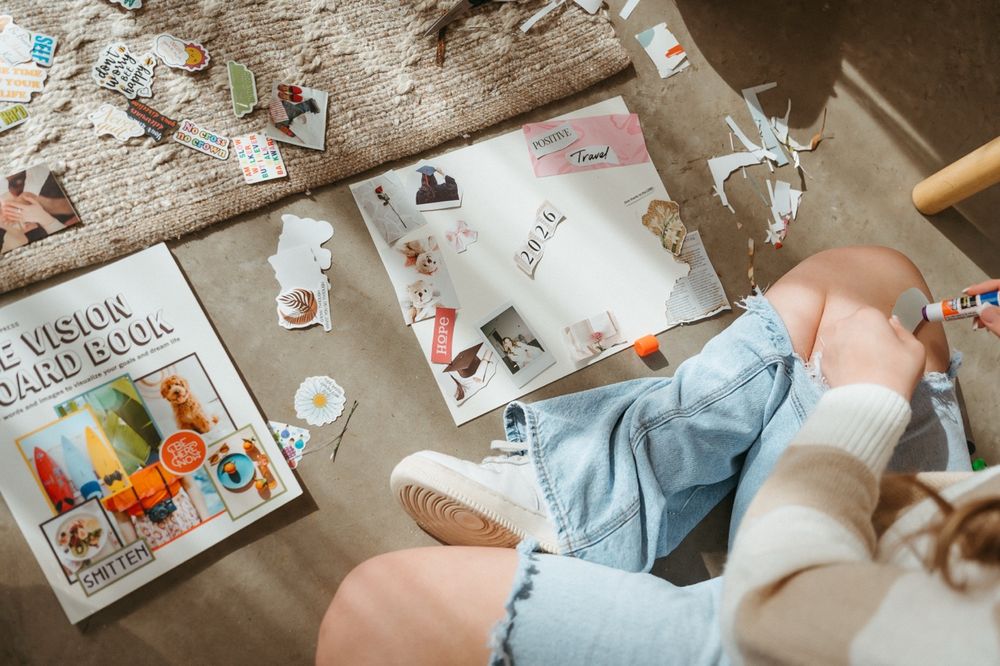 Watercolor painting supplies and art materials laid out on a wooden surface with scattered paint brushes and papers.