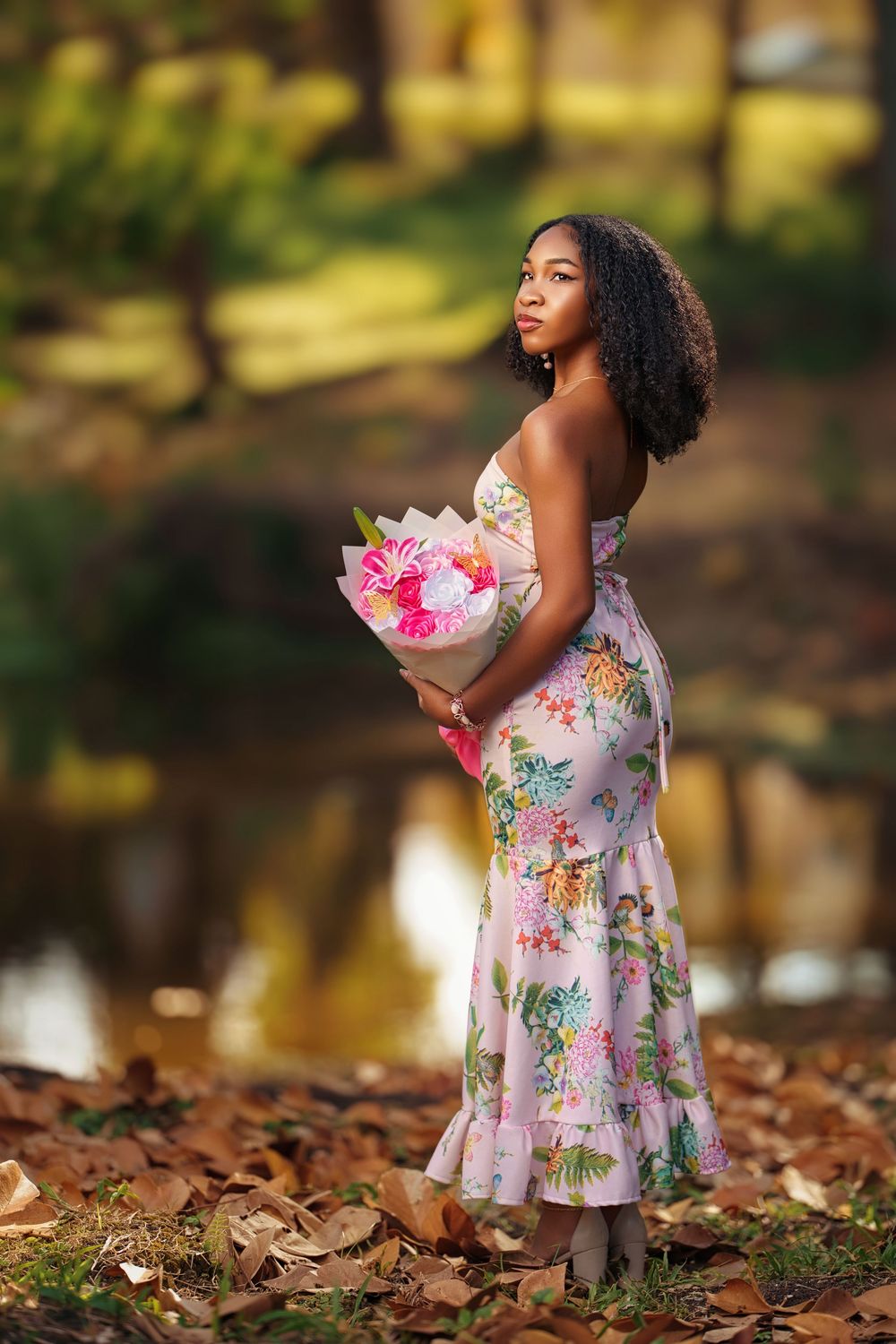 A young girl in a floral dress poses thoughtfully among autumn leaves in a sunlit outdoor setting.