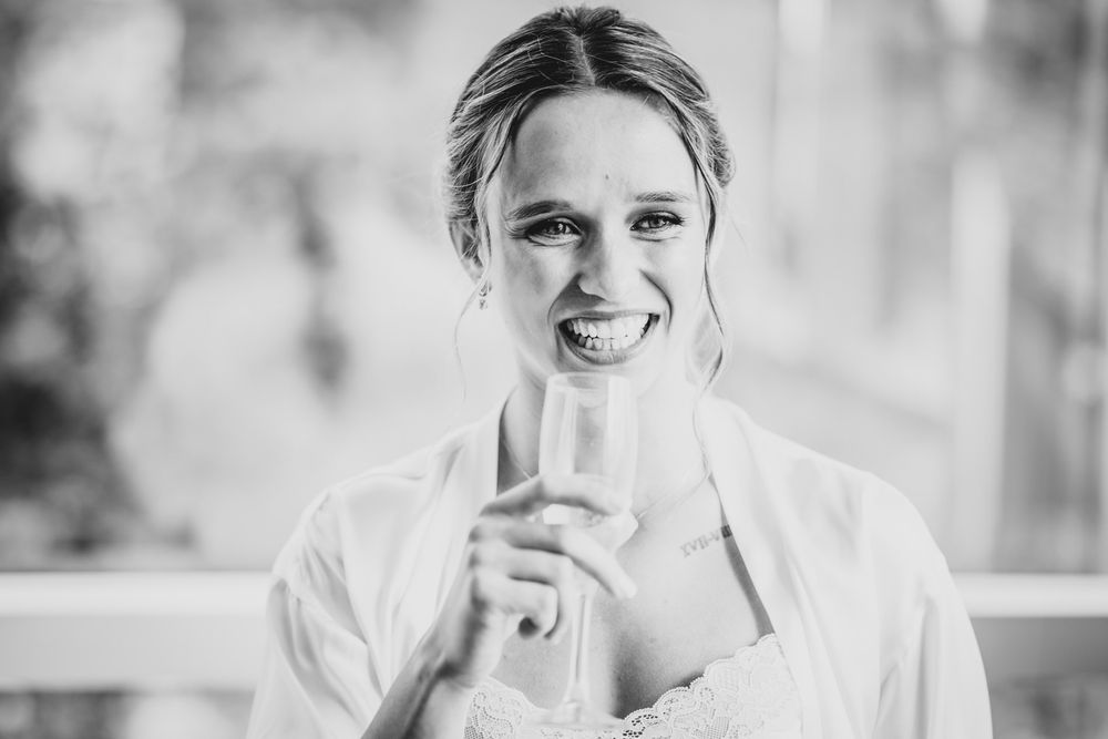 Retrato de la novia sonriendo mientras brinda con una copa durante los preparativos de la boda.