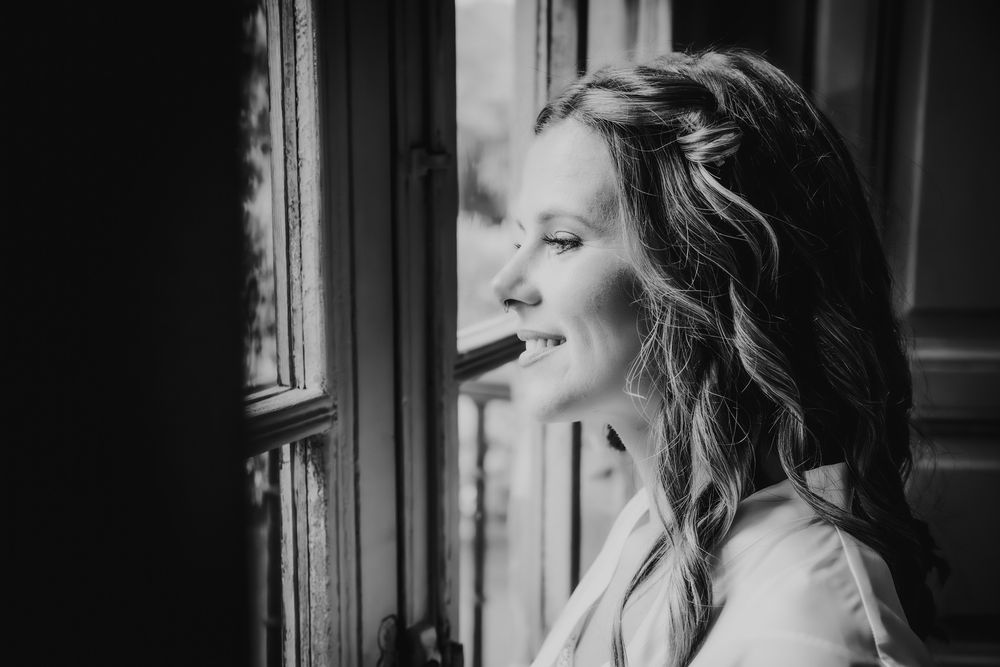 Retrato de la novia mirando por la ventana, preparativos de boda en blanco y negro.
