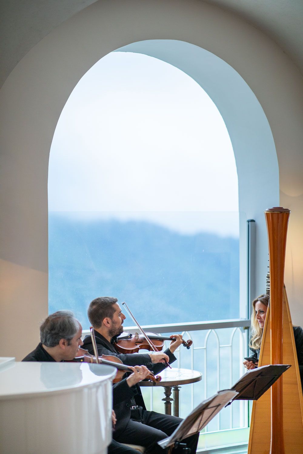 Italian wedding musicians play, set against jaw dropping view through archway of Amalfi coast